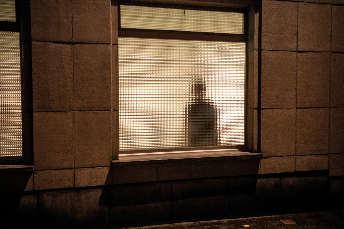 Silhouet van een persoon achter een verlicht raam met geribbeld glas in Brussel