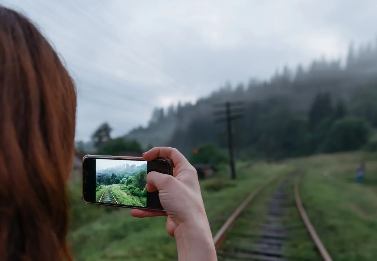 Person photographs a railway line in a mountain landscape with a smartphone