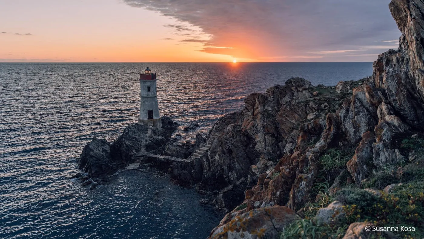 Lighthouse on rocky coast at sunset over sea