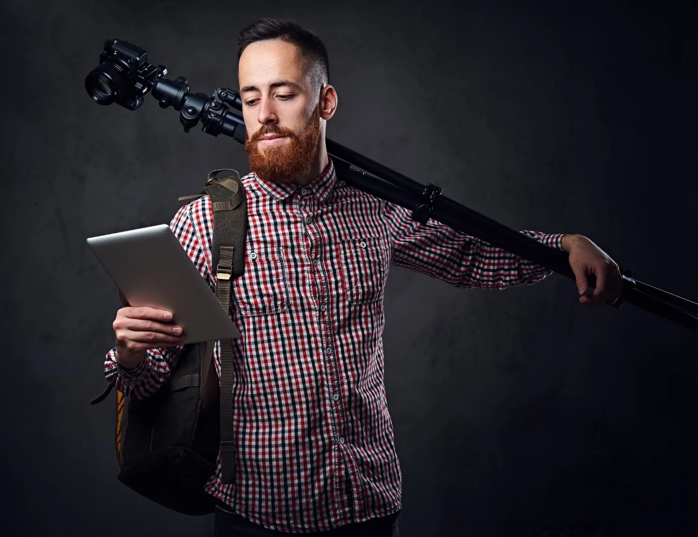 Photographer carries a tripod over his shoulder and holds a tablet