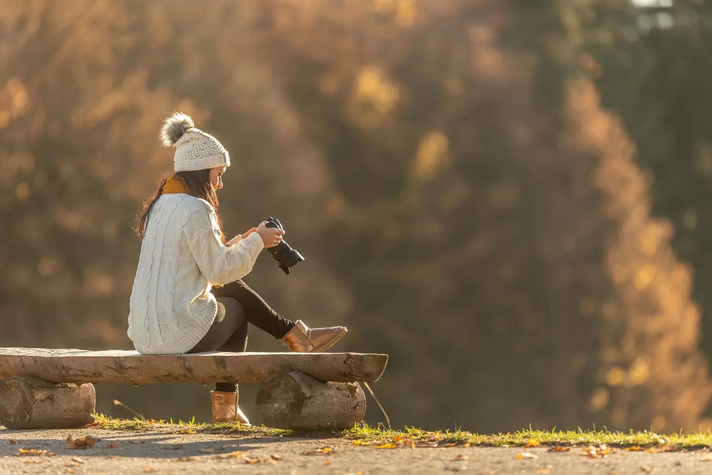Woman with camera sits on a wooden bench in warm autumn light