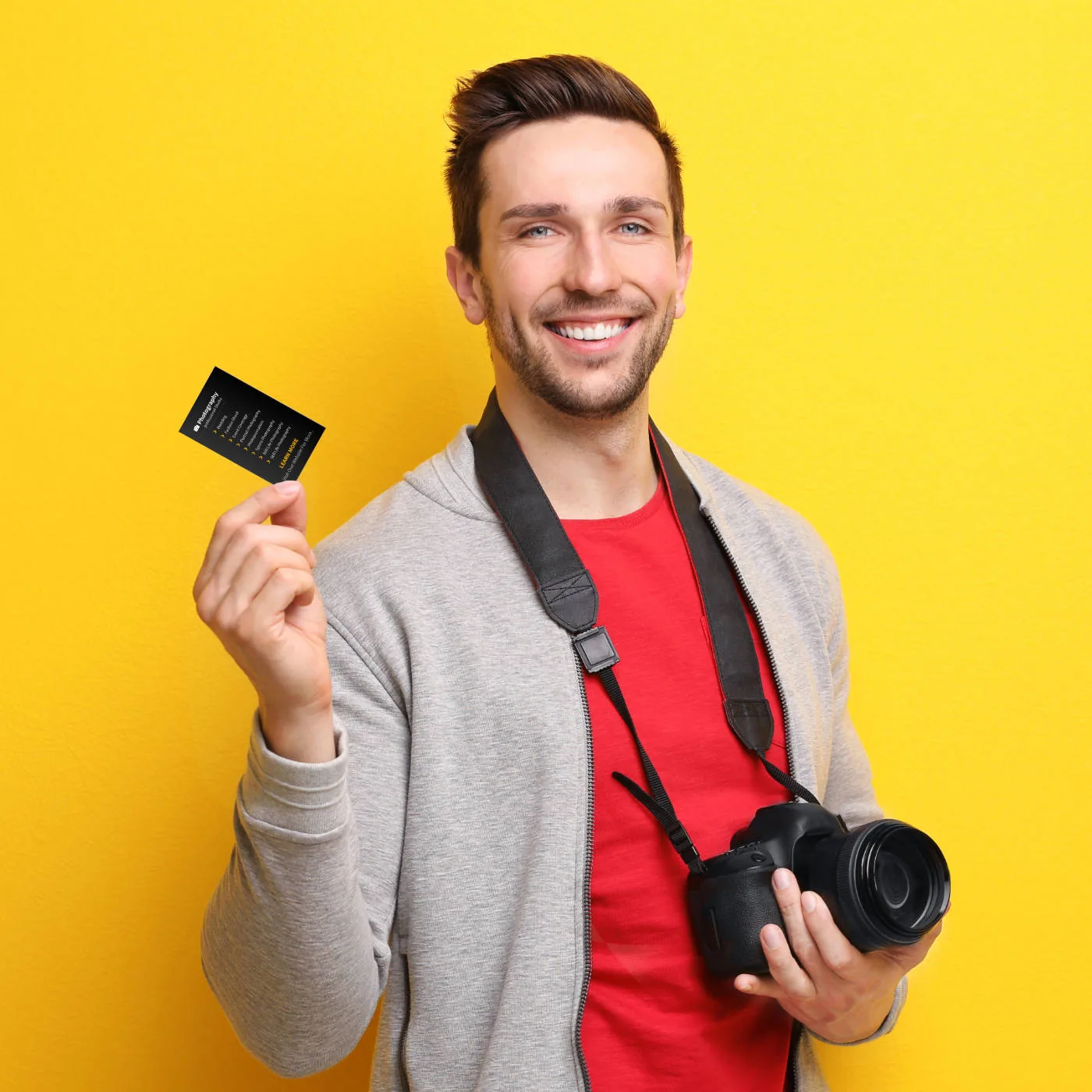 Smiling photographer with camera and memory card against a yellow background