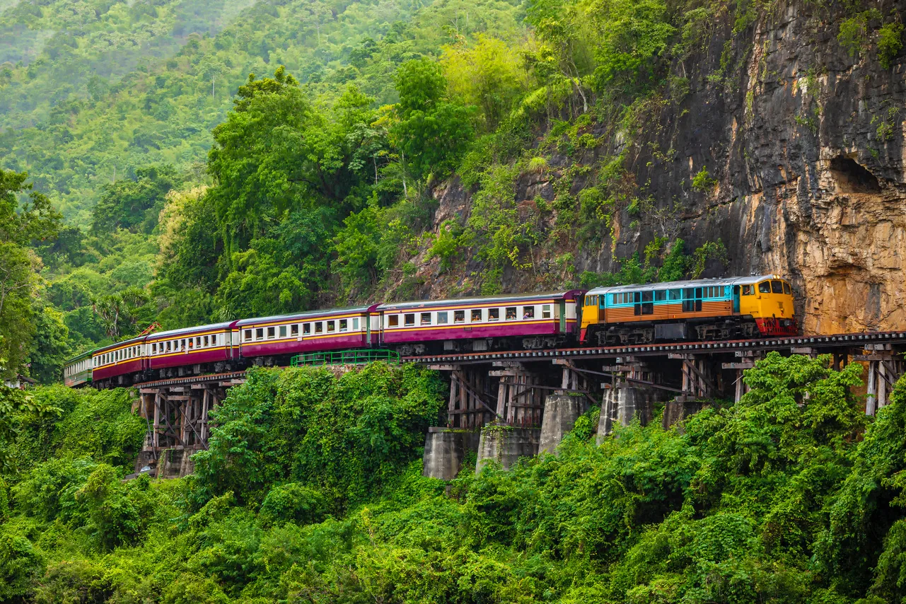 Kleurrijke trein op de beroemde Death Railway brug langs tropische jungle in Thailand
