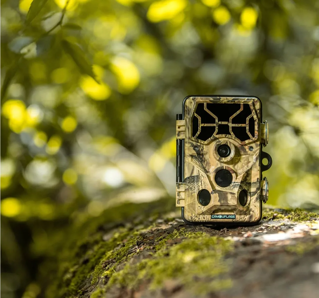 Wildlife camera with camouflage pattern on a mossy tree trunk in the forest