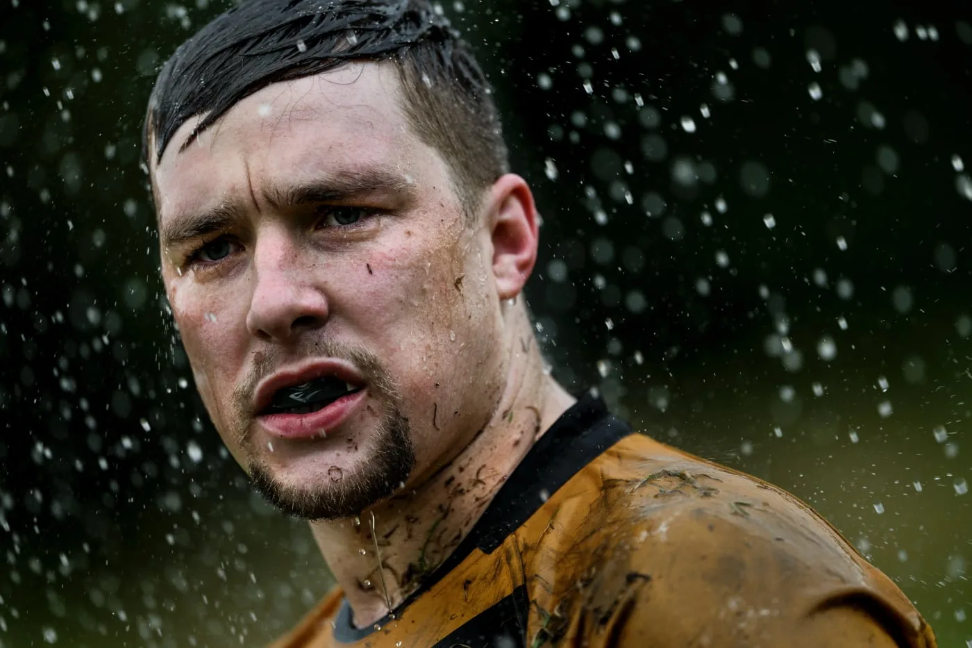 Close-up of a mud-covered athlete in the rain, with water droplets visible
