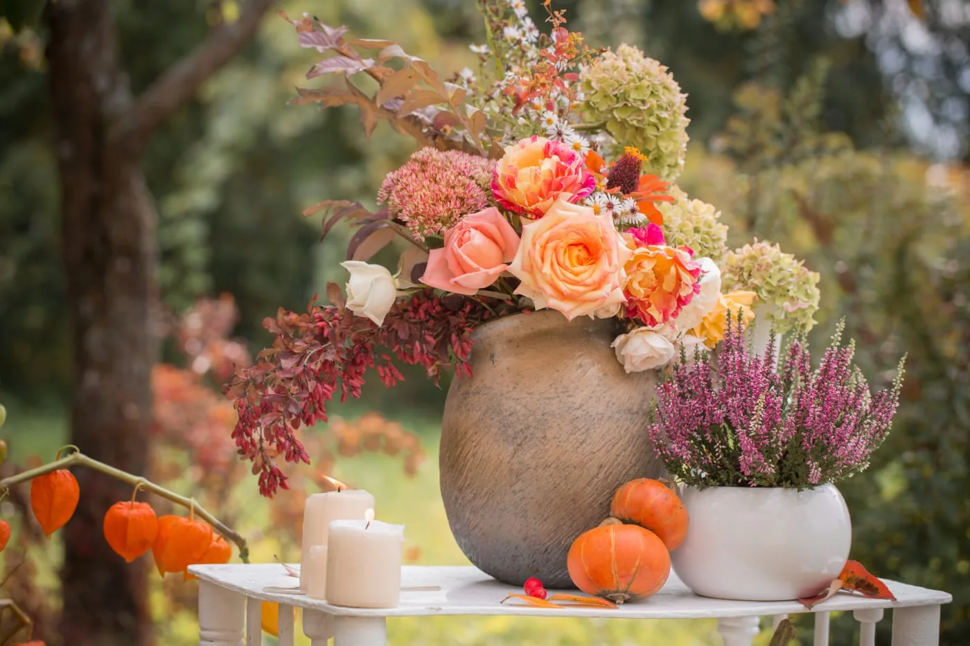 Autumn bouquet with roses, hydrangeas, heather, pumpkins, and candles in a garden