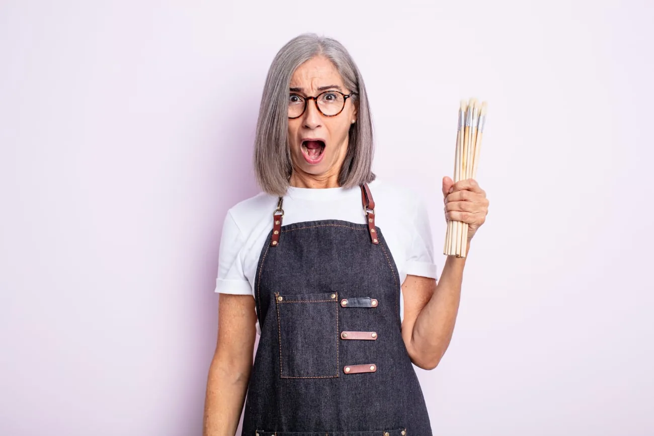 Surprised older woman with painter's apron and brushes