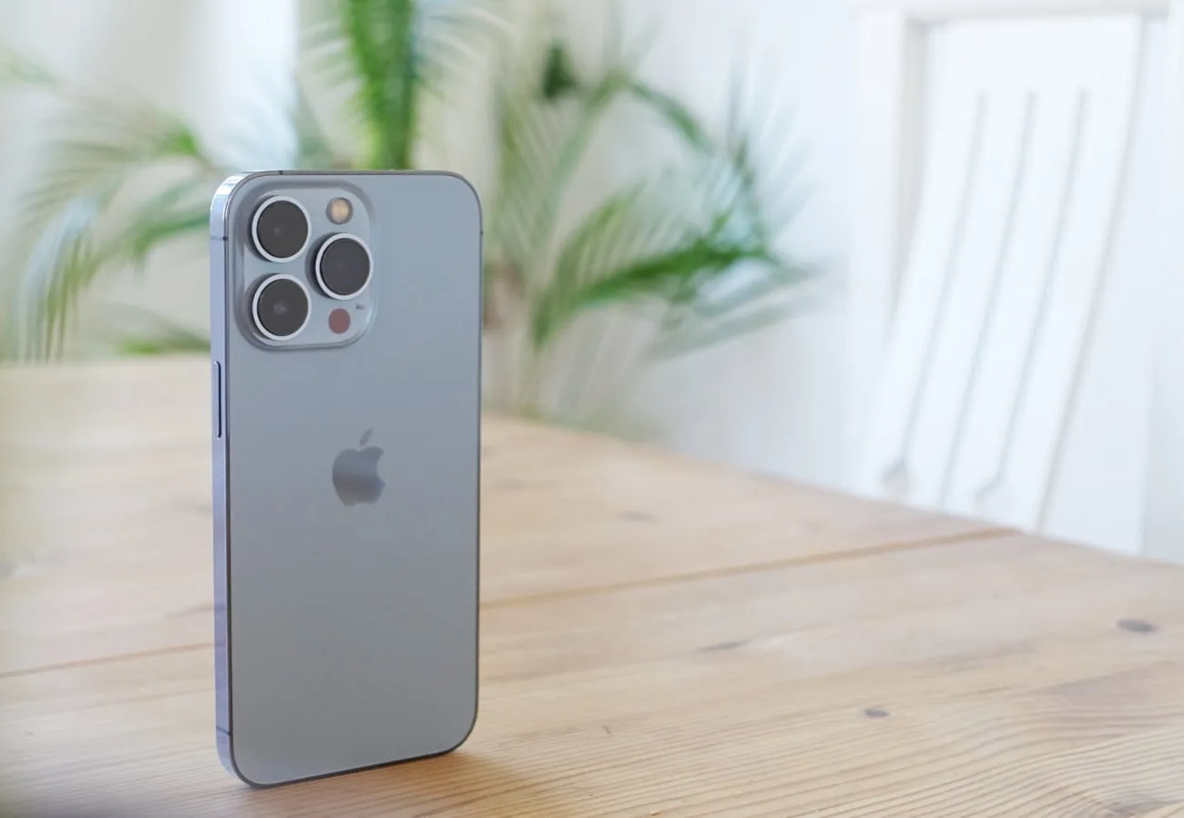 iPhone stands upright on a table with blurred background with a plant
