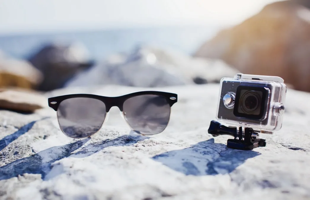 zonnebril en GoPro op rots met uitzicht op zee