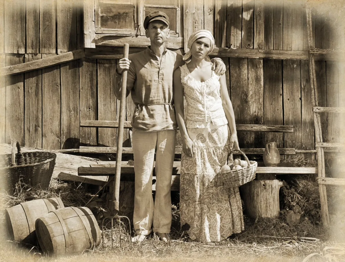 Old sepia photograph of a man and woman in front of a wooden barn