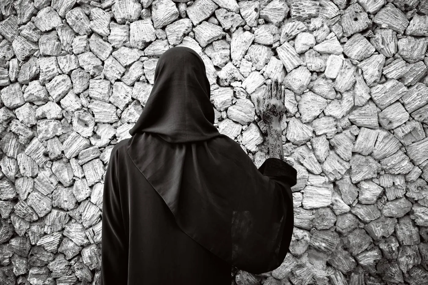 © Annelies Damen - Fikra, vrouw in zwart gekleed met zwart hoofddoek staat met rug naar camera tegen een muur met hand op muur