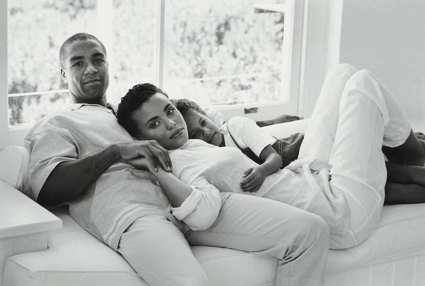 man, woman, and child lying on a sofa in black and white