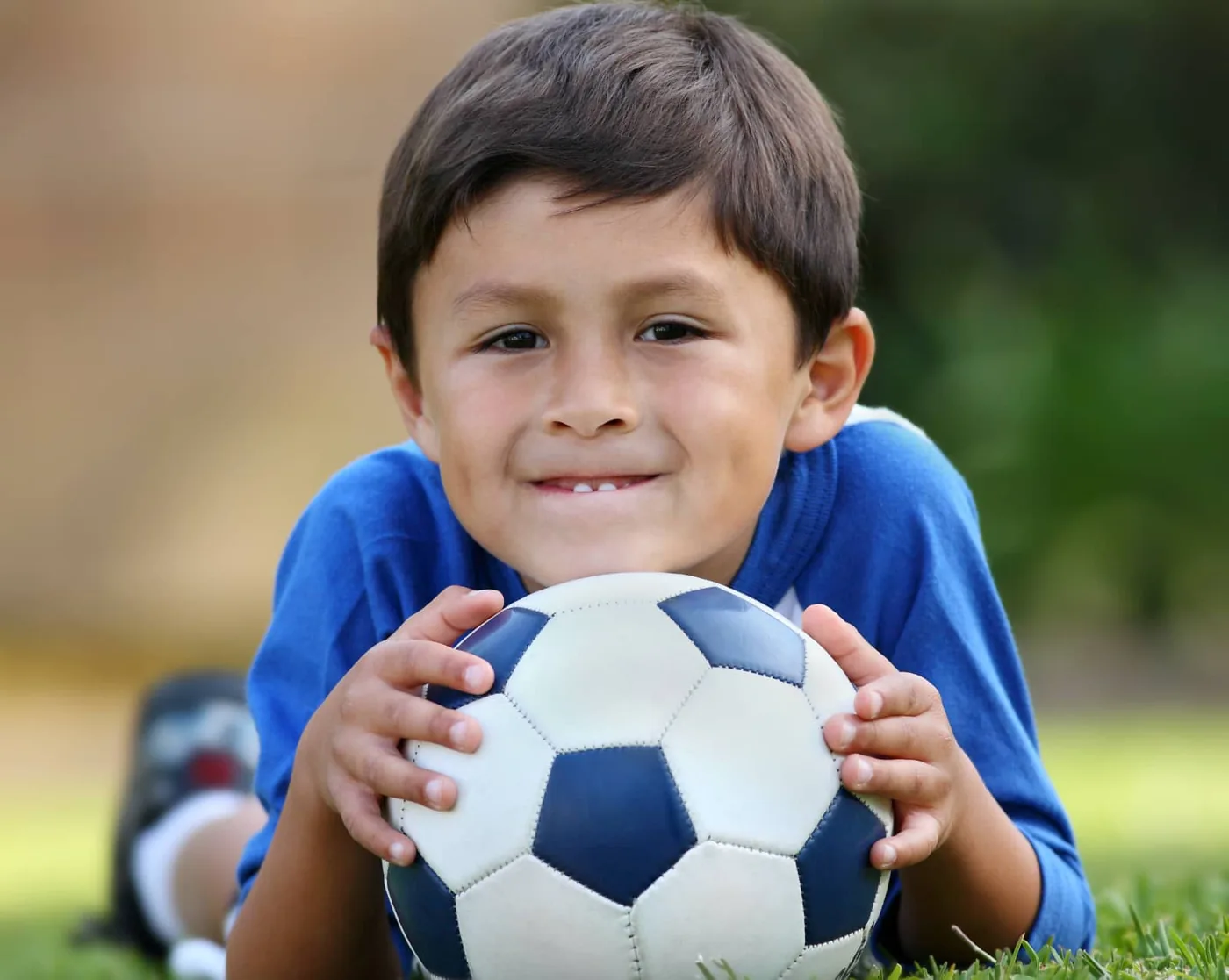 boy lying on his stomach with a soccer ball under his chin