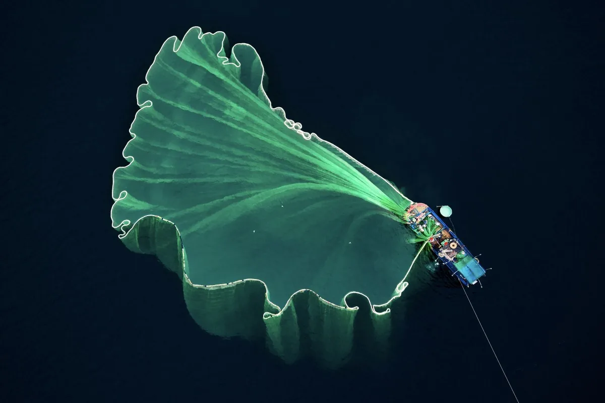 Fishing boat with a large fan-shaped fishing net at sea, photographed from above in Vietnam.