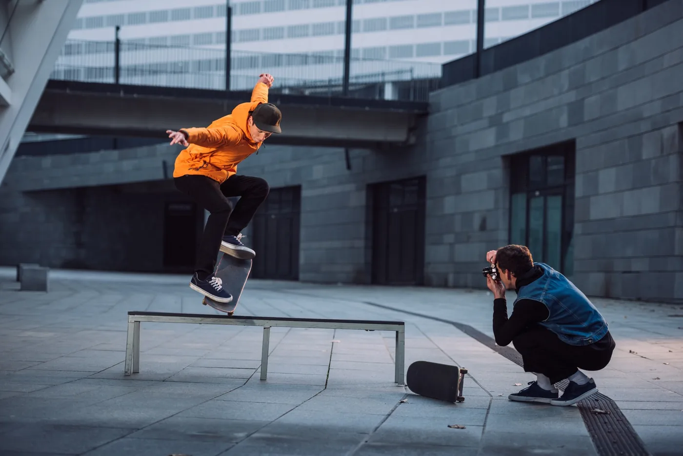 foto van een fotograaf die een skater fotografeert die met zijn plank op een bankje balanceert