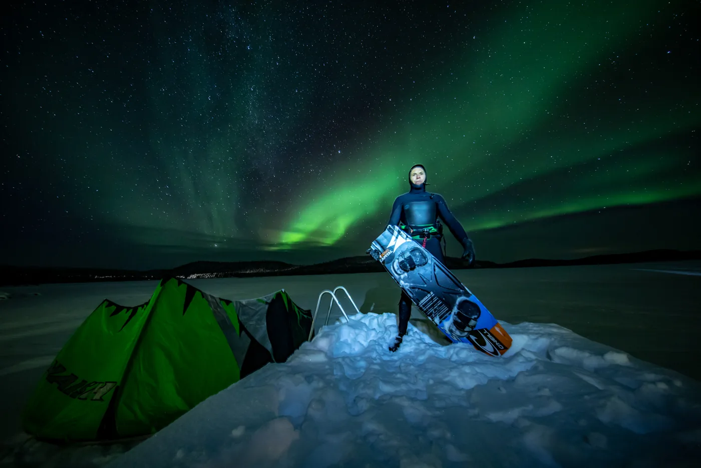 Kitesurfer met board in de sneeuw onder het noorderlicht tijdens de Noordkaap Challenge