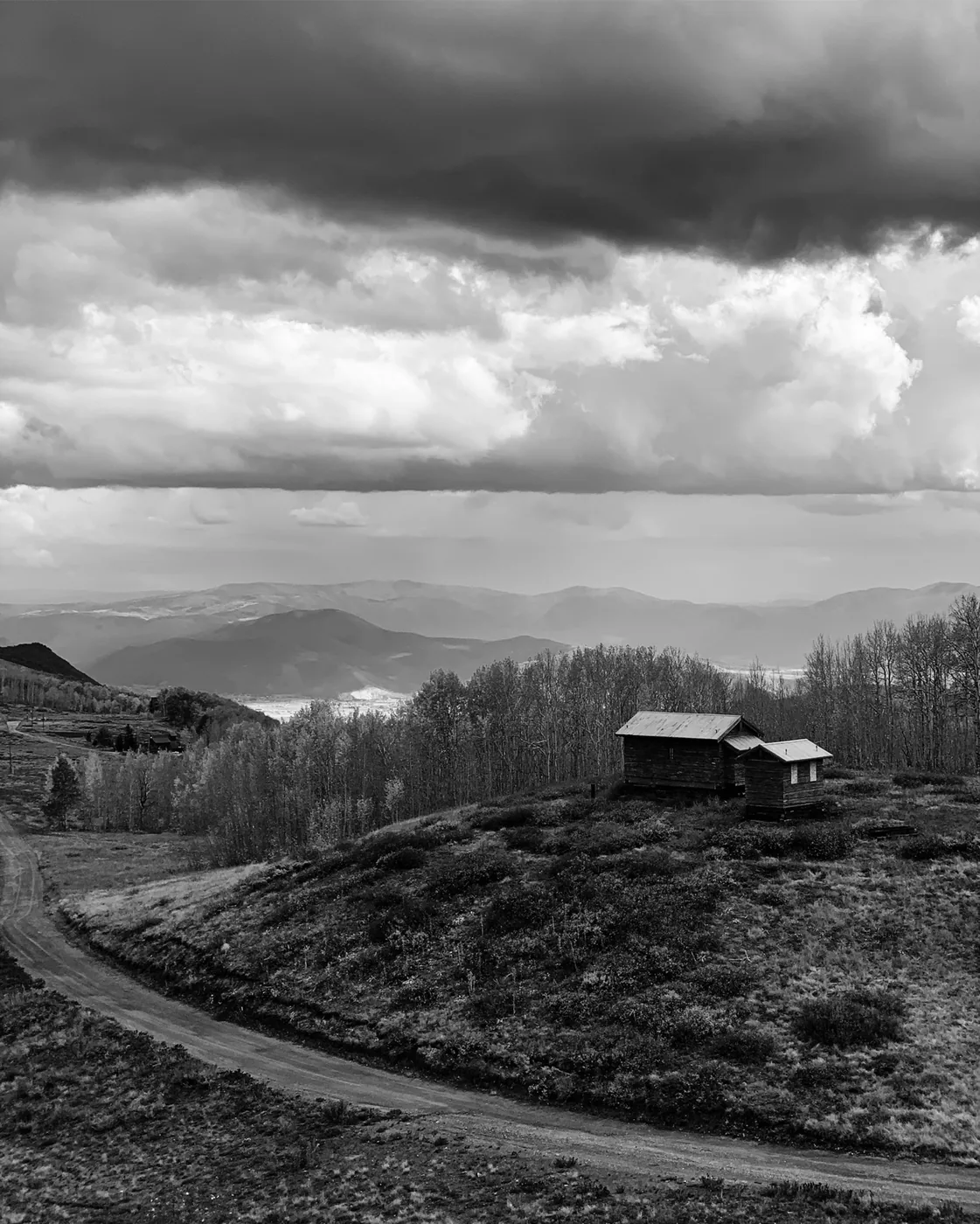 Black-and-white mountain landscape with a hill, barn, trees, and dark clouds