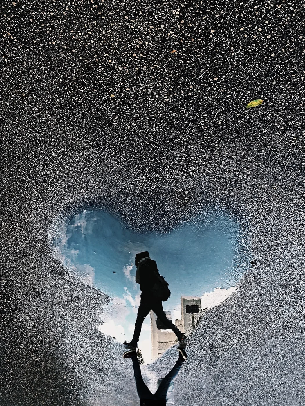 Heart-shaped puddle on asphalt reflecting a person walking