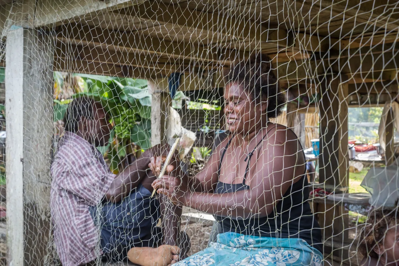 Woman repairing a fishing net with a man beside her