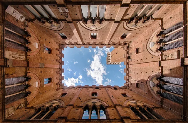 architectuurfoto van de binnenplaats van het Pallazzo Publico (Stadhuis) van Siena, Italië. Recht naar boven kijkend worden de patronen en symmetrie in de architectuur fraai benadrukt