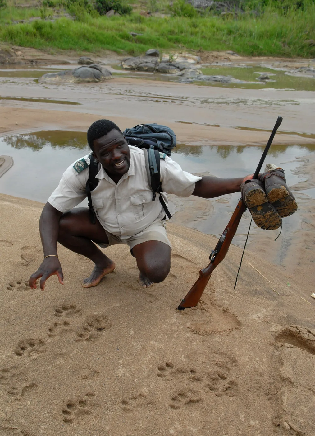 ‍foto: Tom van der Leij van landschap Zuid-Afrika met reisgids geknield en met geweer in handen en schoenen uit in handen