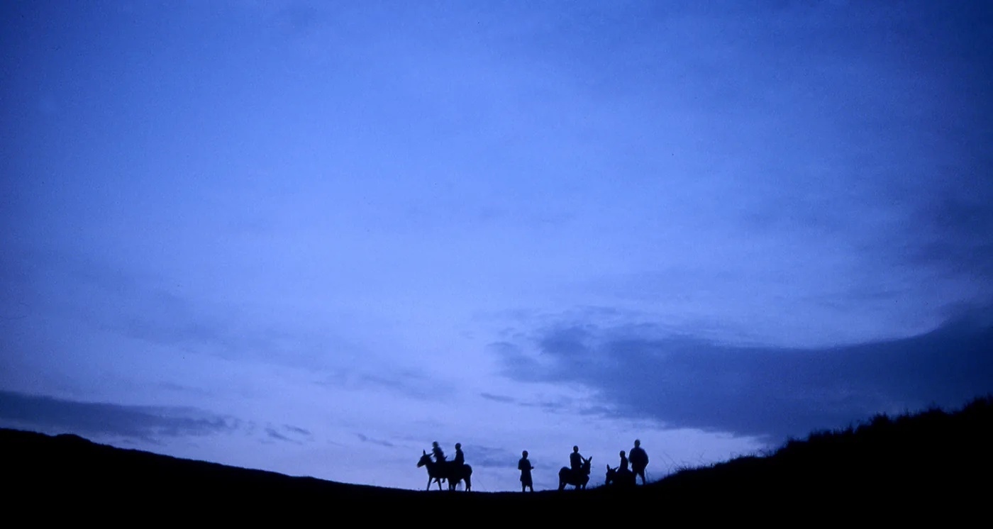 Mannen op paarden in verte op heuvel als silhouet met blauwe avondlucht