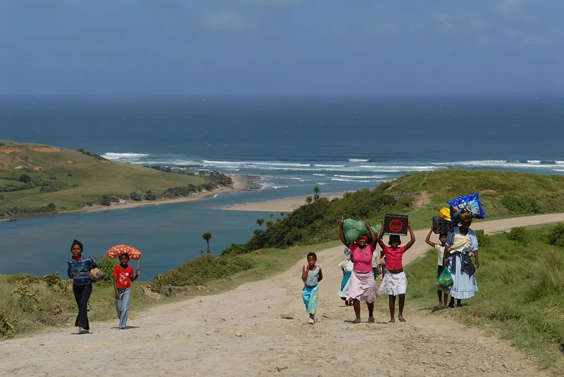 Zuid-Afrika - Wild Coast, vrouwen en kinderen lopen langs kust met goederen op hoofd