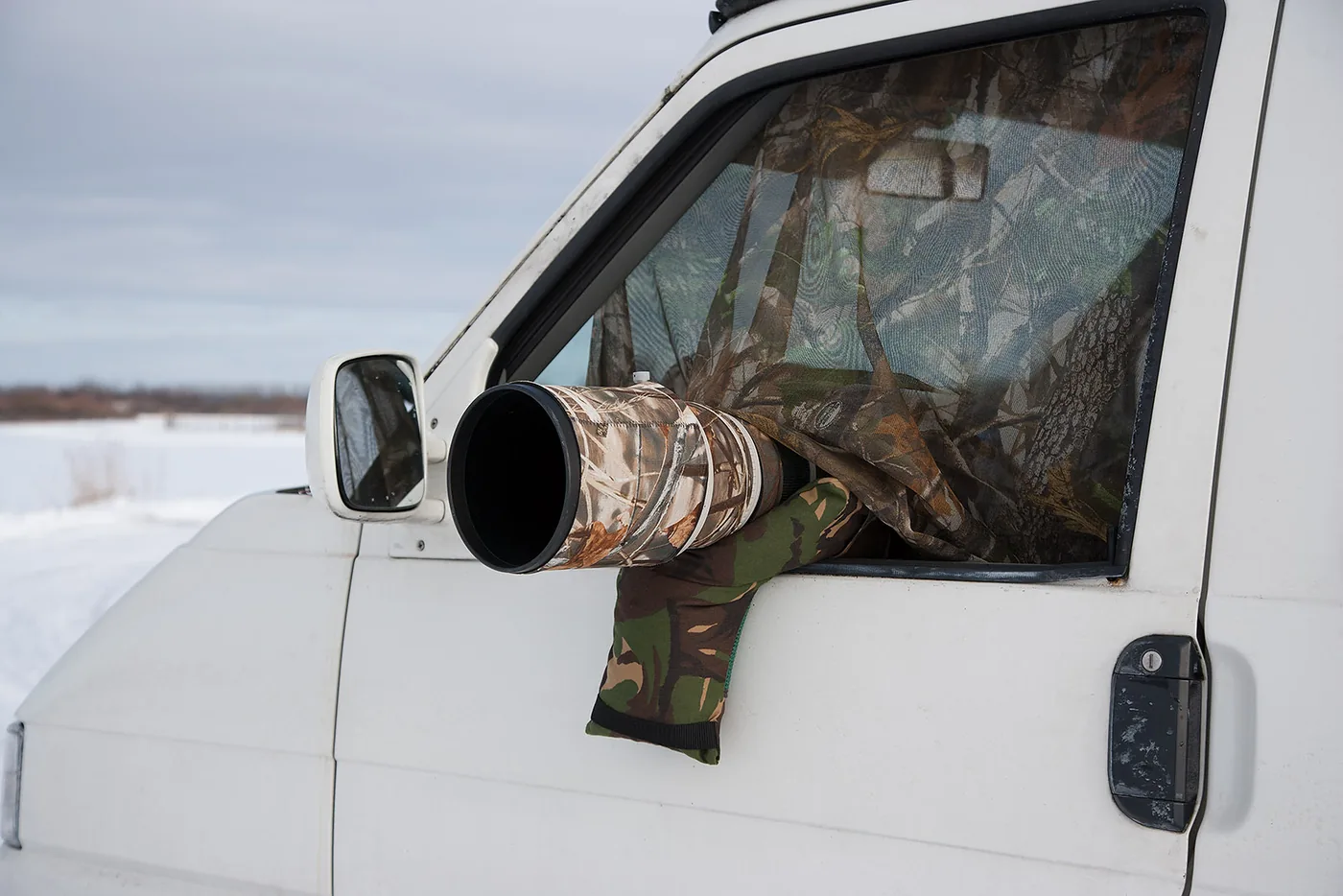 foto van wit busje met camouflagedoek voor het raam en een cameralens die uit voorraam steekt ook gecamoufleerd