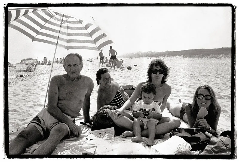 Family sits under an umbrella on the beach in a black and white photo