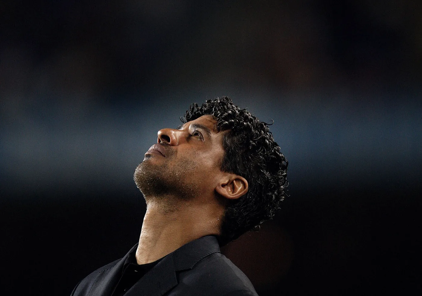 Close-up of a soccer coach looking thoughtfully upward during an evening match in a stadium