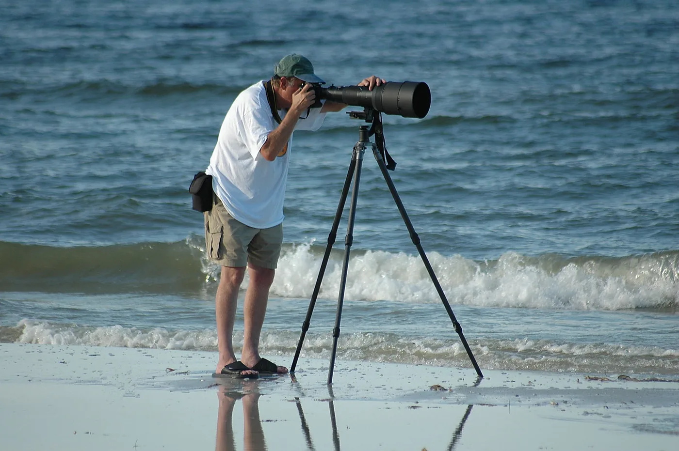 Man using a telephoto lens on a tripod by the sea