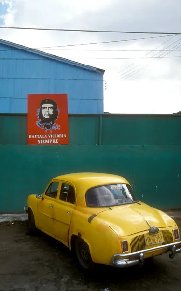 Polychromatic use of vivid, busy color areas: a yellow Cuban car by a fence with a red poster