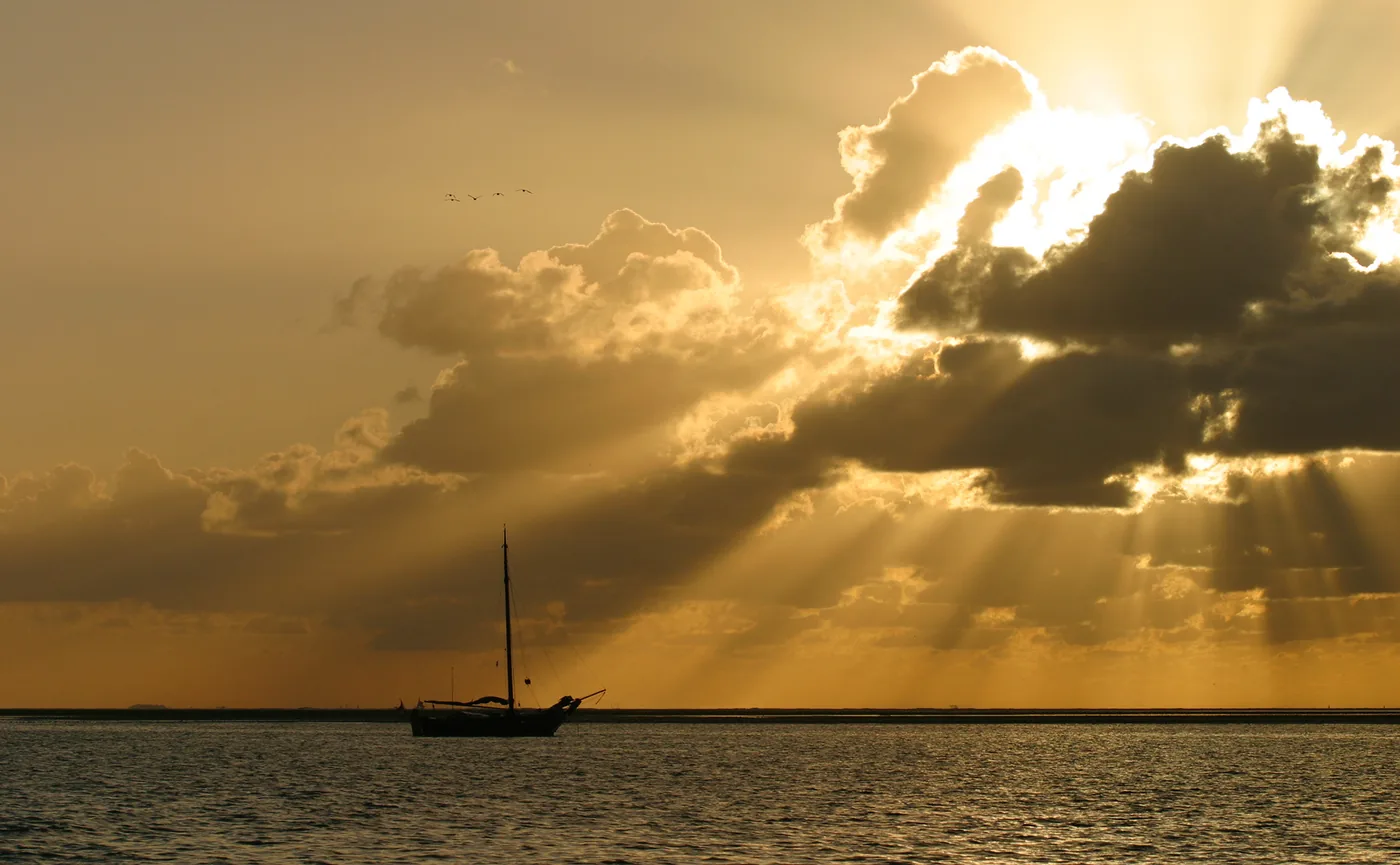 Sailboat on the Wadden Sea beneath dramatic clouds and rays of sunlight