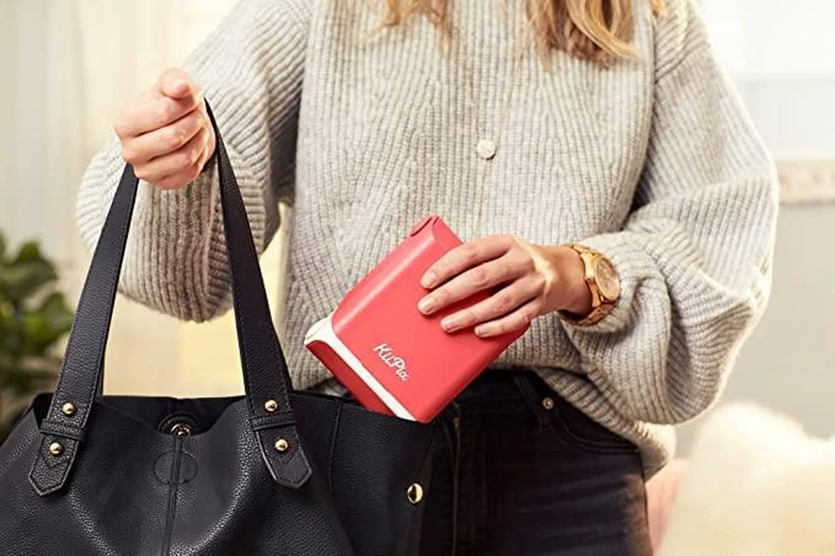 Woman placing a mini instant printer and smartphone in a handbag