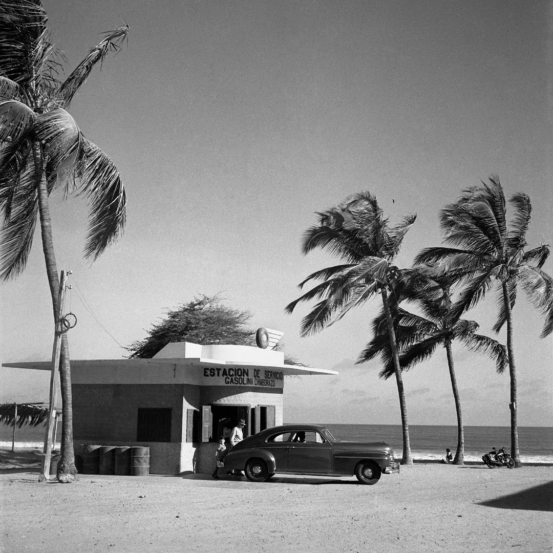 Tankstation met klassieke auto en palmbomen aan de kust van Playas in Ecuador in 1960