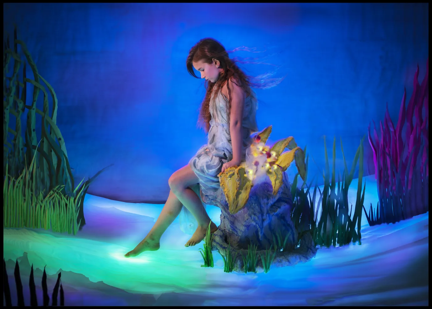 Woman sits in a colorful illuminated setting with water plants