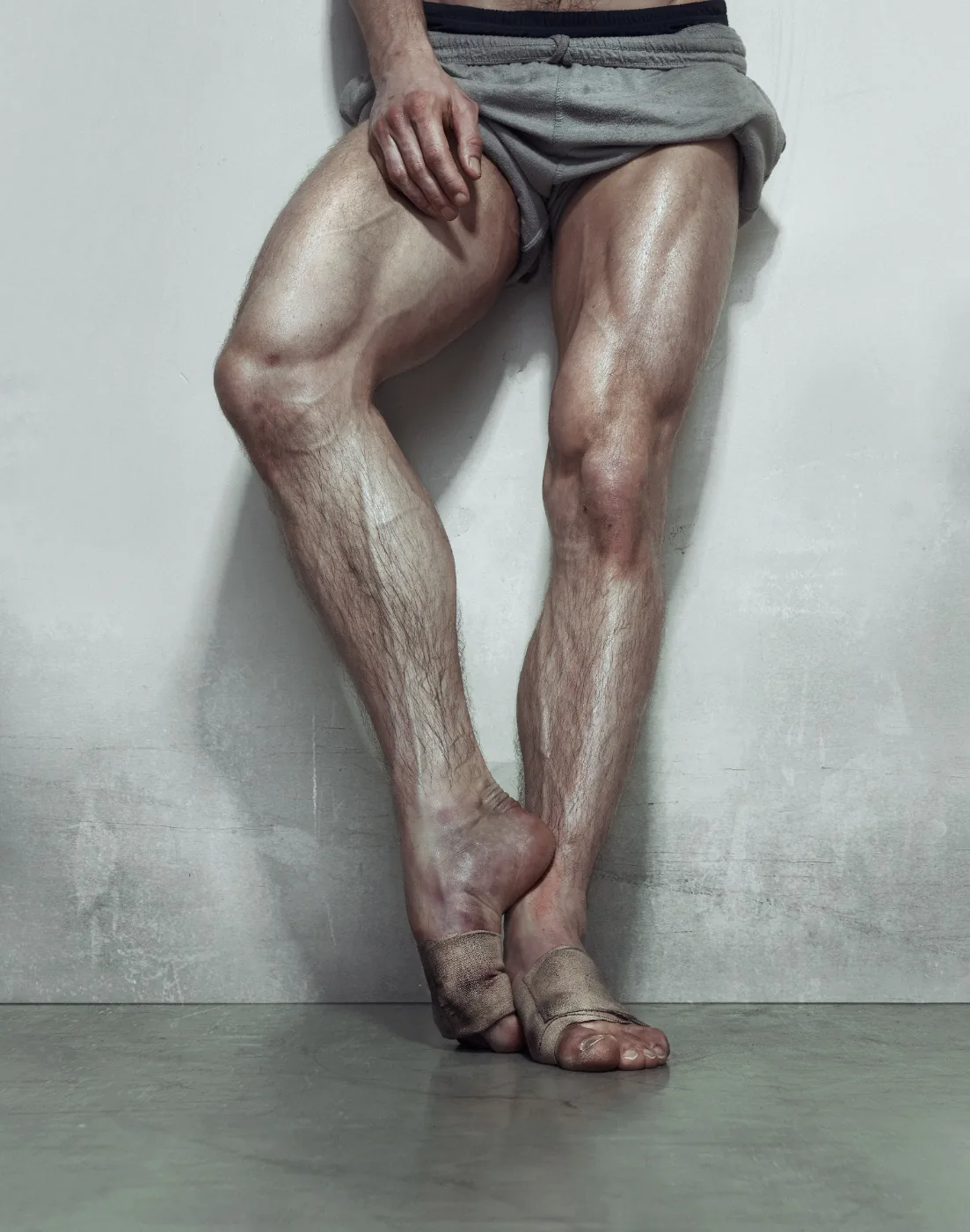 Detail of a male dancer’s legs in shorts, with crossed feet and taped ankles, from Erwin Olaf’s Nederlands Dans Theater series (2009)