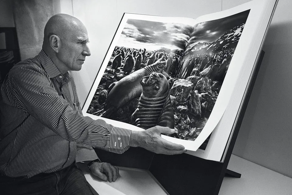 foto van Sebastião Salgado zittend bij grote uitgave van zijn boek Genesis