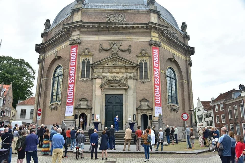 Voor een ronde kerk staan bezoekers bij de ingang, met aan de gevel twee verticale World Press Photo-spandoeken.
