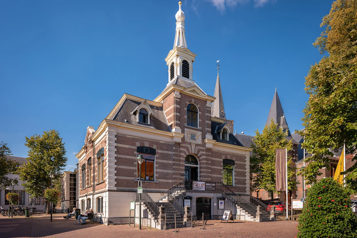 Bakstenen gebouw van Fotomuseum Hilversum op een zonnig plein onder blauwe lucht, met een banner naast de trap.