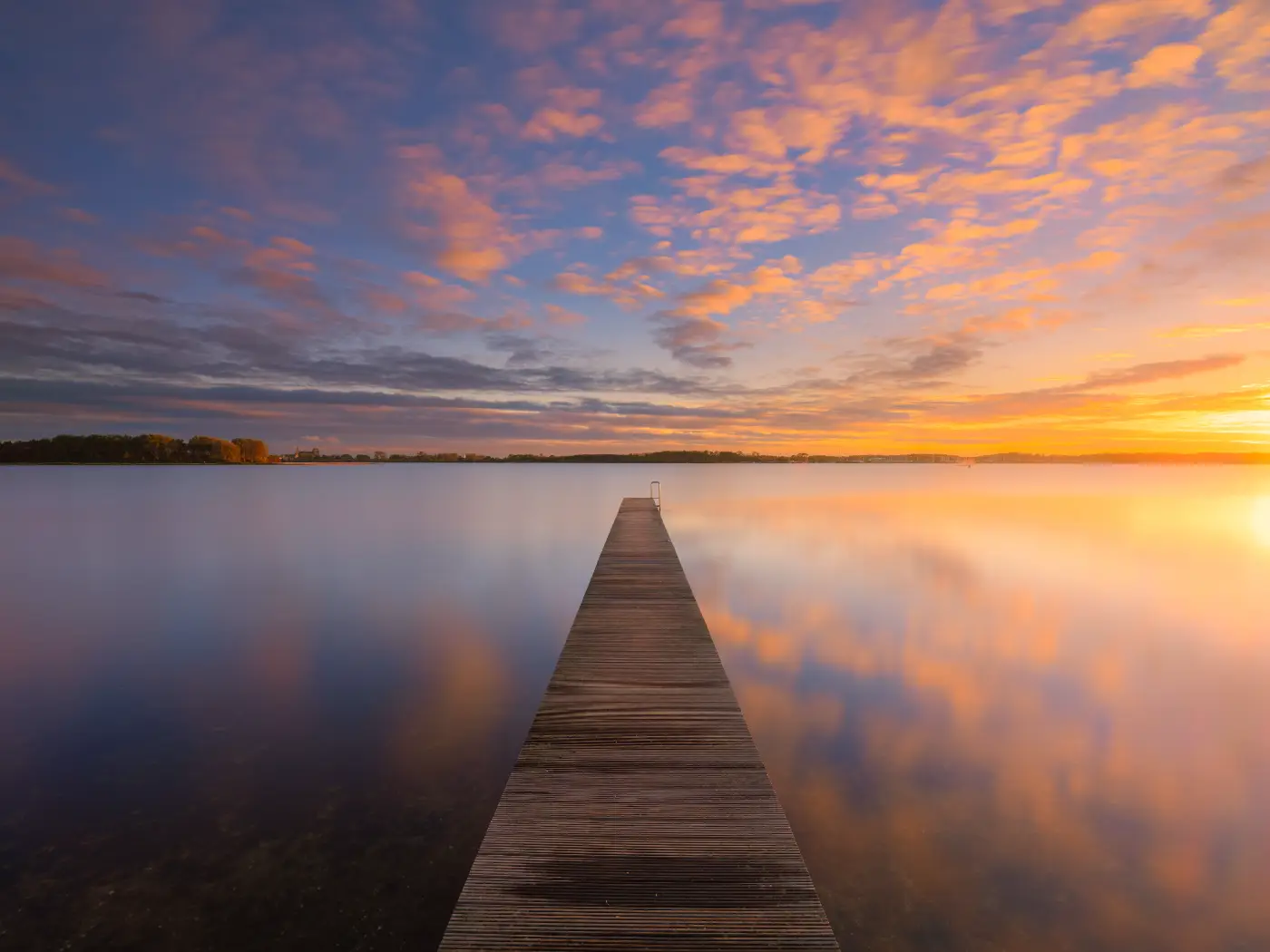 Wooden jetty over still water beneath a colourful evening sky
