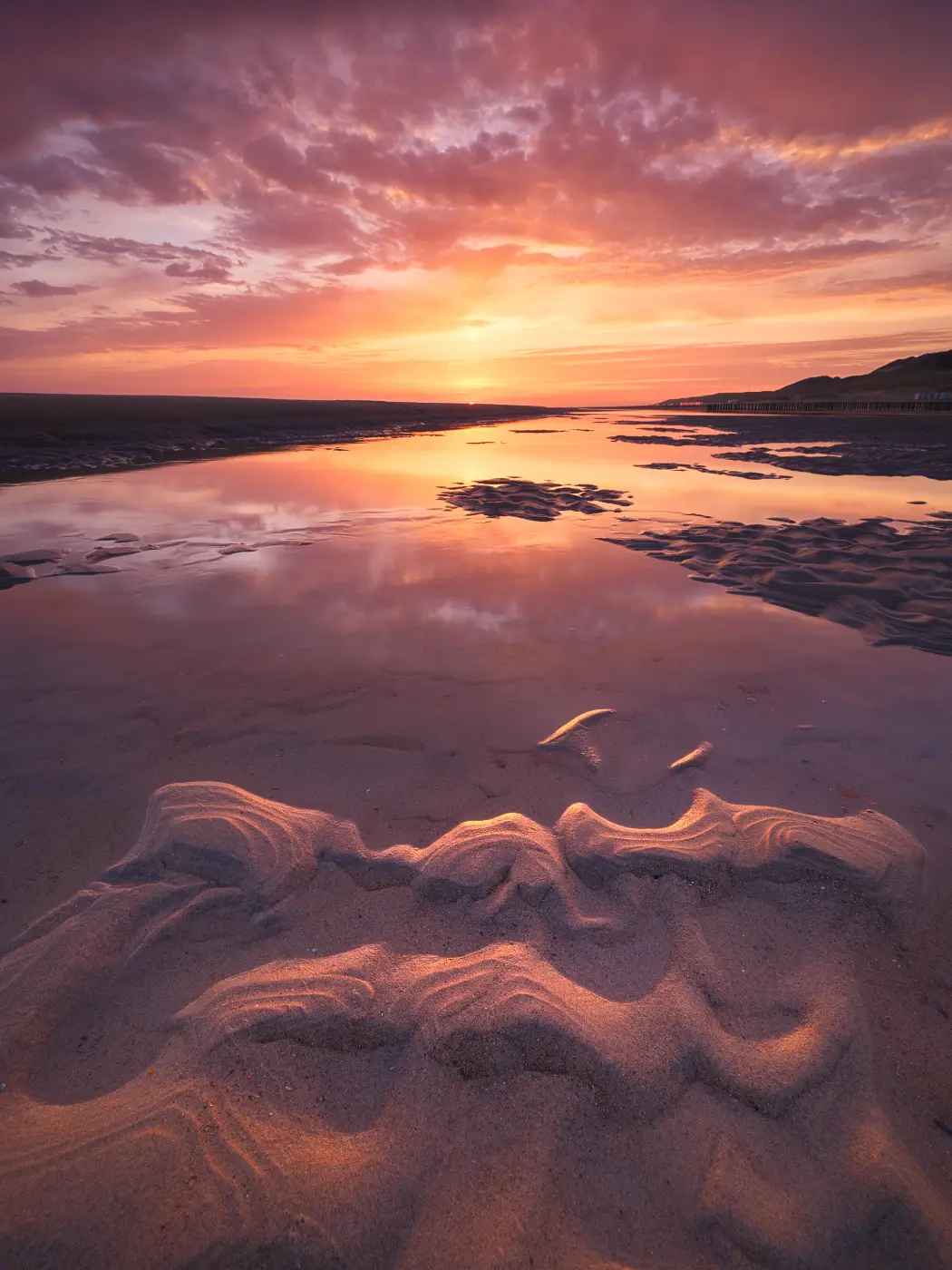 Coastal landscape with wet sand beneath a colourful sunset