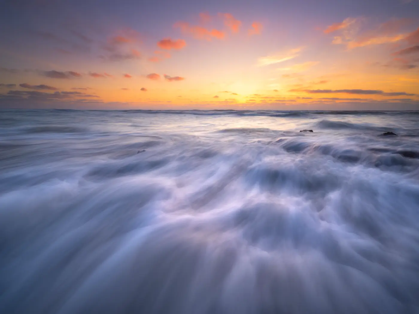 Sea with long, flowing water movement beneath a colourful evening sky