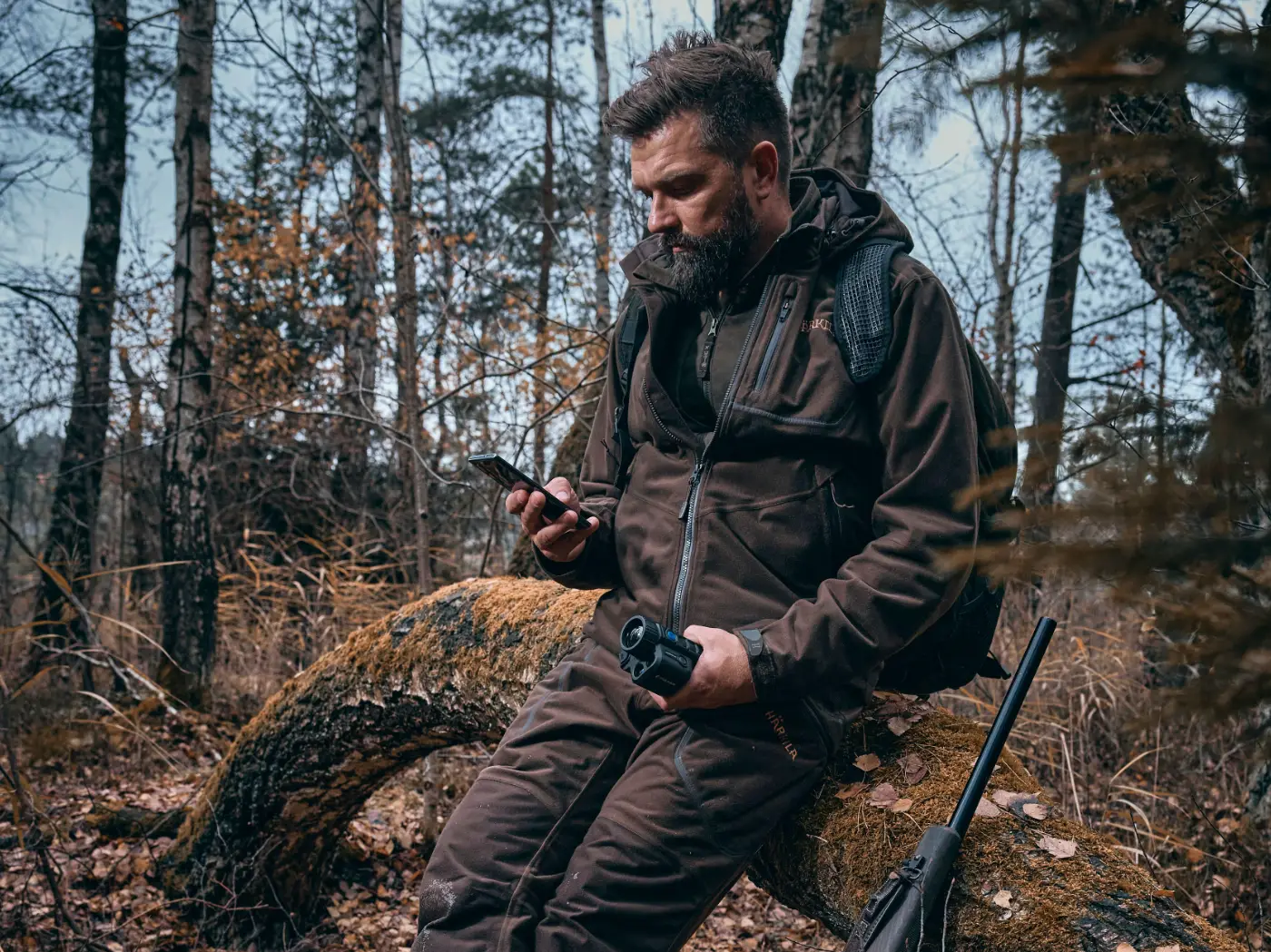 Man in een bos gebruikt een handheld warmtebeeldkijker om dieren op te sporen.