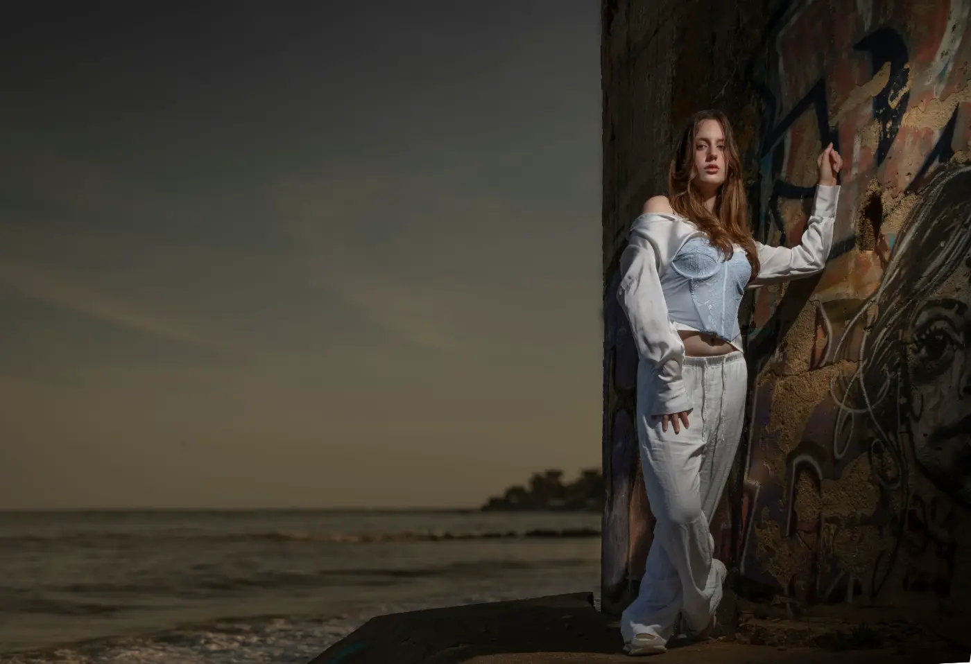 Portret van een vrouw in witte kleding bij een graffitimuur, belicht met off-camera flitslicht