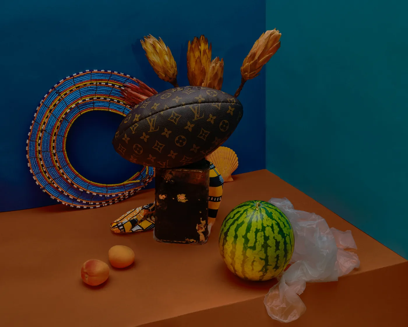 Fotografisch stilleven met een kralencirkel, een bedrukte etui, gedroogde bloemen en fruit tegen blauwe wanden van Maya Inès Touam.