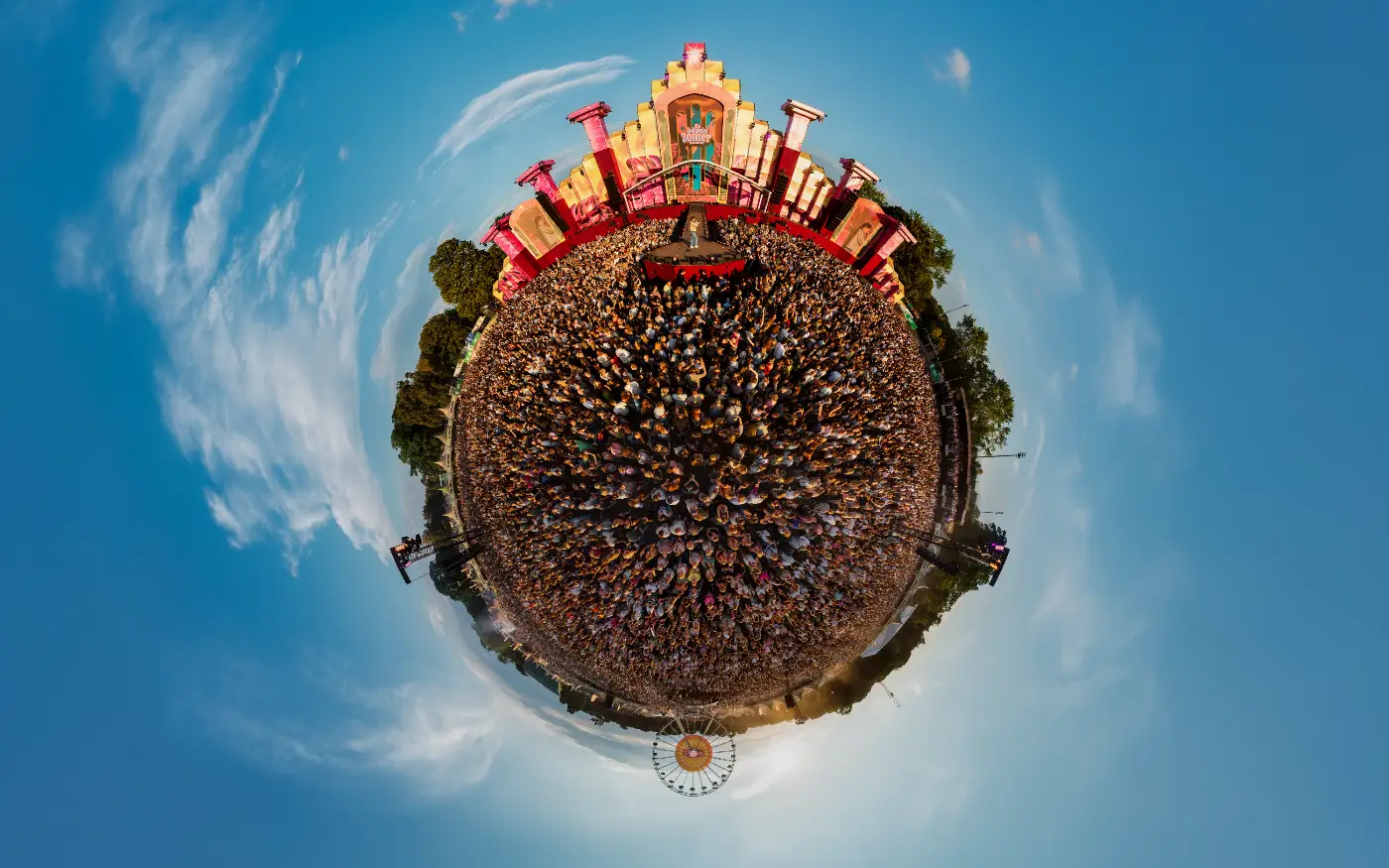 Fisheyeopname van een groot festivalpubliek rond een podium in little-planet-perspectief.