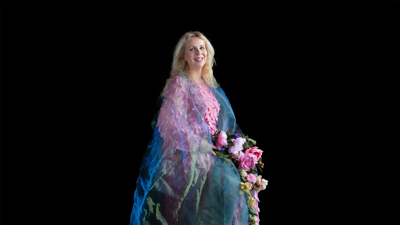 Marleen Kant met roze bloemen tegen een zwarte achtergrond, gefotografeerd door Carla van de Puttelaar voor Zij maakt het verschil.