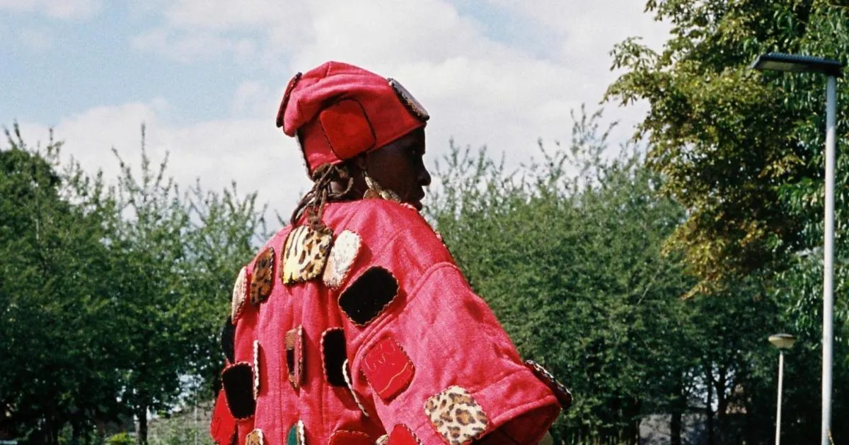A person wearing a red hat and a red cape decorated with patterned patches, photographed by Vincen Beeckman for Parade.