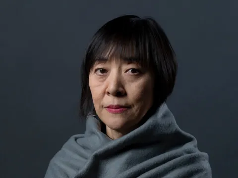 Portret van kunstenaar Chikako Watanabe, gewikkeld in een grijze omslagdoek tegen een donkere achtergrond, door Gert Jan van Rooij.